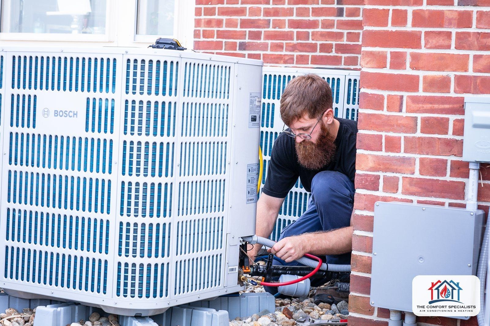 A technician works on an outdoor heat pump unit next to a brick wall in Central Massachusetts A technician works on an outdoor heat pump unit next to a brick wall in Central Massachusetts