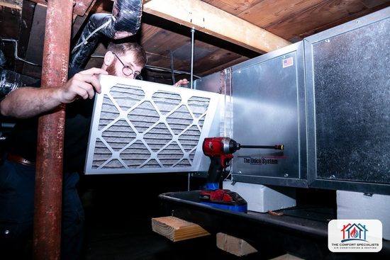A technician changes the filter on a compact air handler in a Central Massachusetts basement